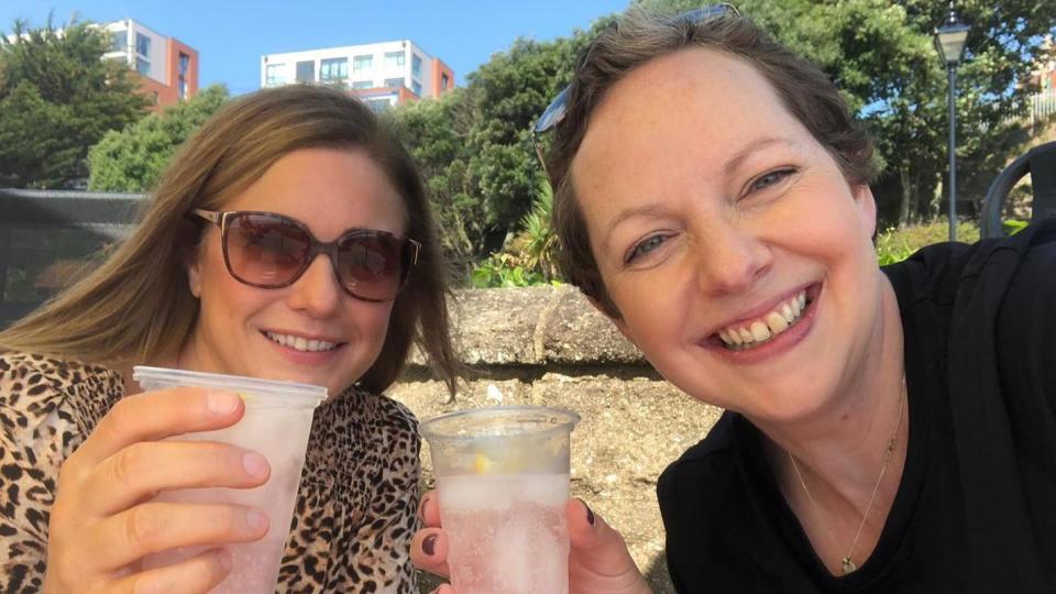 Two woman holding plastic cups filled with drinks, smiling at the camera