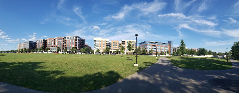 A wide view of a grassy park with a path, surrounded by modern apartment buildings under a clear sky