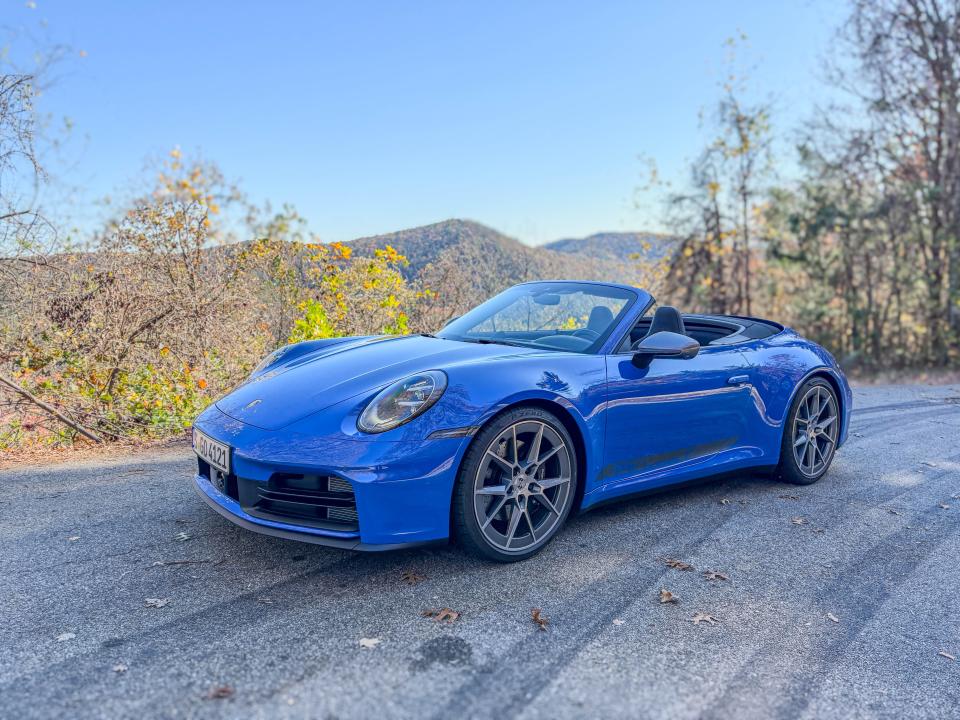 A blue 2025 Porsche 911 Carrera T Cabriolet with the top down parked on the side of the road.