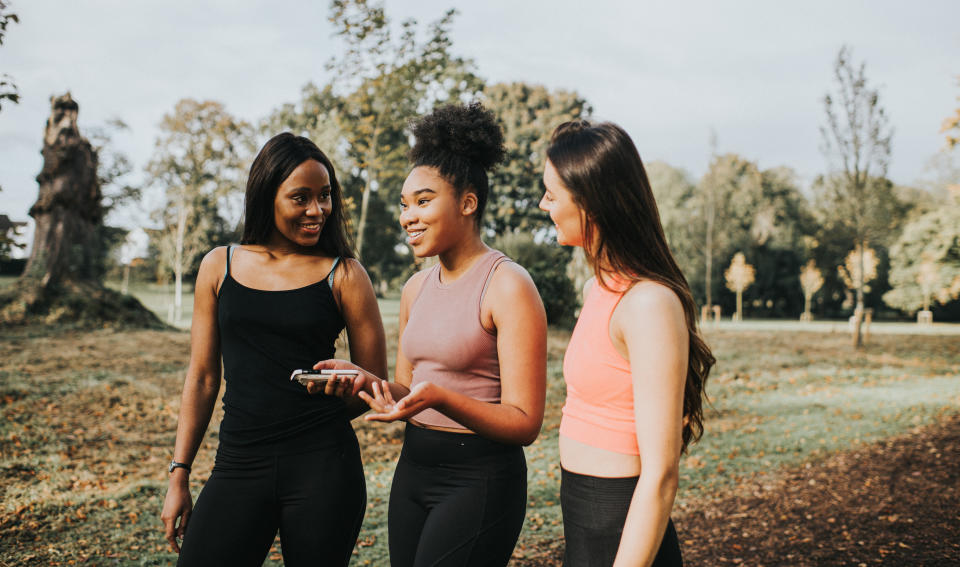 Three women in activewear chatting and smiling while walking in a park