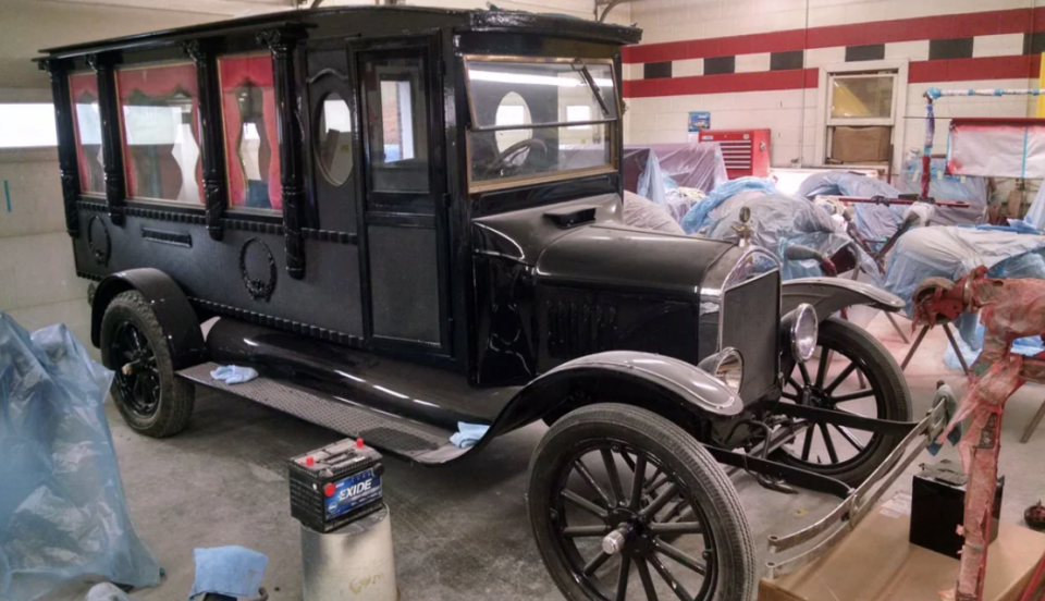 Vintage black hearse undergoing restoration in a garage, surrounded by tools and equipment