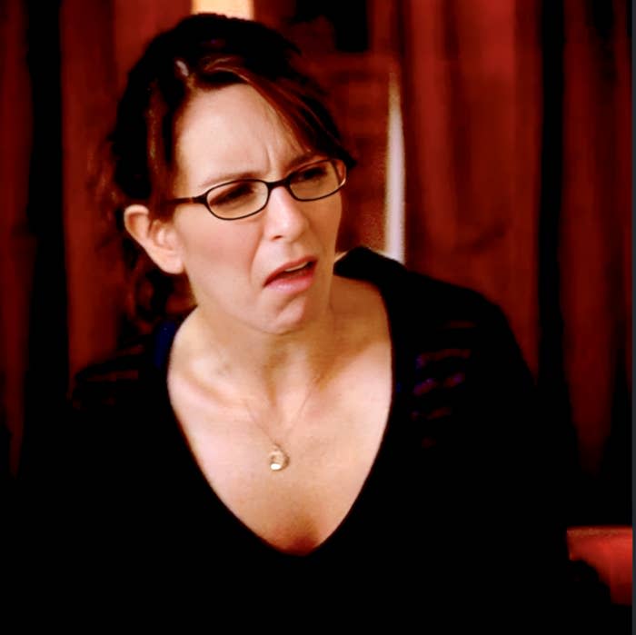 Person with glasses and a puzzled expression, wearing a black top in an indoor setting