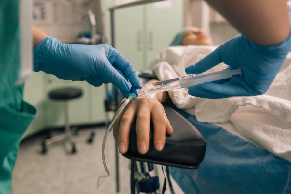 Medical professional prepares to administer an IV drip to a patient lying on a bed in a hospital room