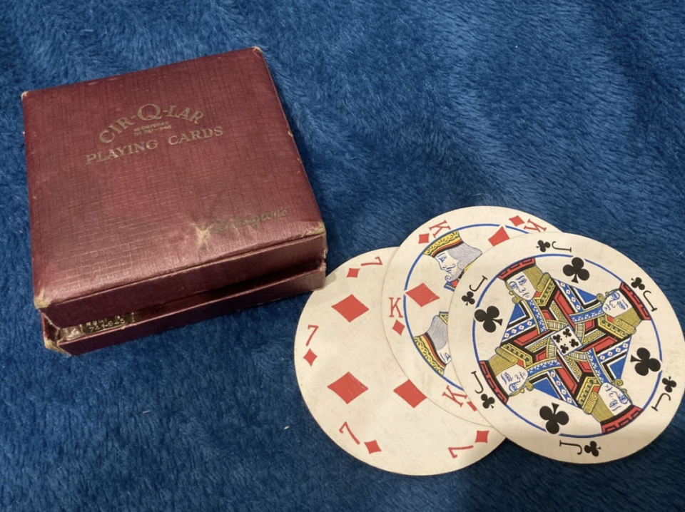 Circular playing cards with kings and a queen next to a red &quot;CIR-Q-LAR Playing Cards&quot; box on a blue surface