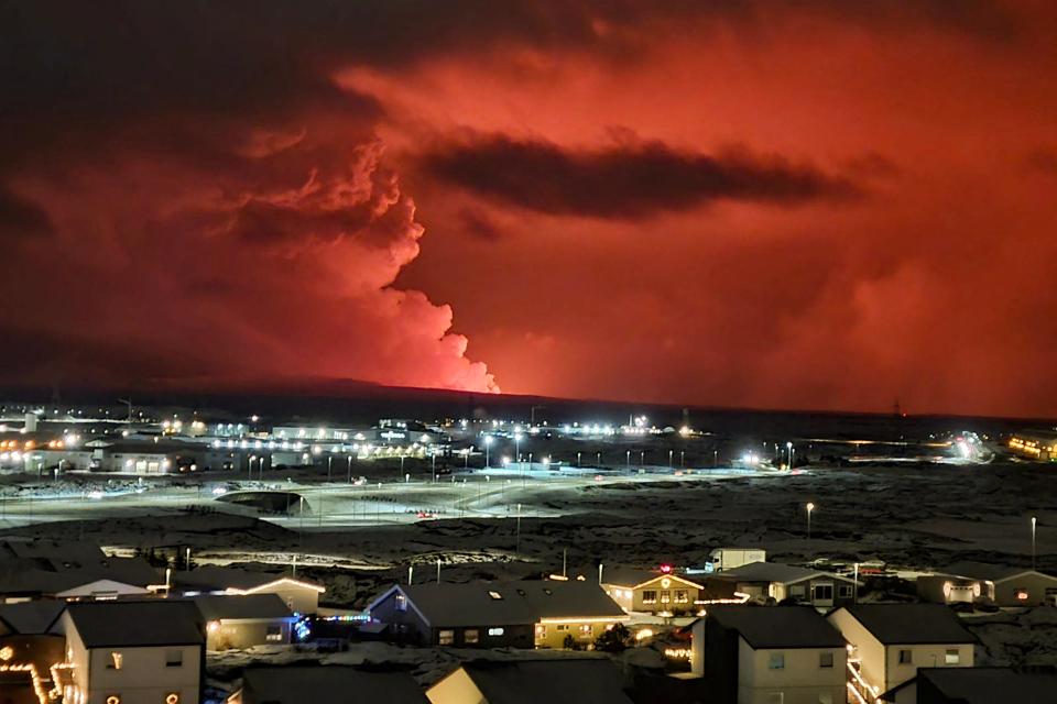 Houses in the village of Hafnarfjordur is seen as smoke is billowing in the distance as the lava colour the night sky orange from an volcanic eruption on the Reykjanes peninsula, western Iceland on December 18, 2023. A volcanic eruption began on Monday night in Iceland, south of the capital Reykjavik, following an earthquake swarm, Iceland&#39;s Meteorological Office reported. (Photo by Oskar Grimur Kristjansson / AFP) (Photo by OSKAR GRIMUR KRISTJANSSON/AFP via Getty Images)