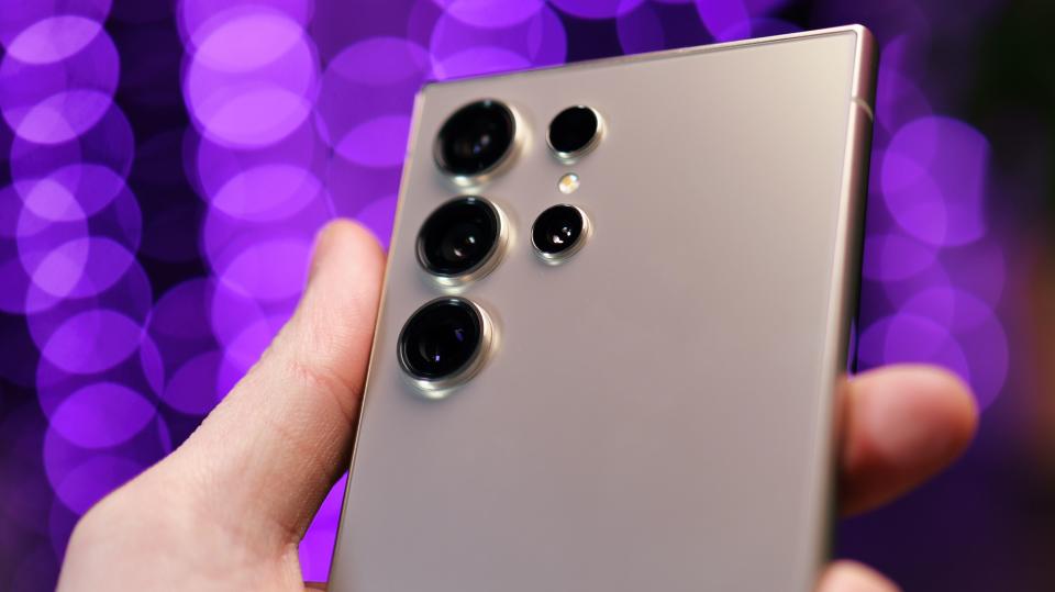 Close up of cameras on a Samsung Galaxy S24 Ultra phone held in a hand with purple lights blurred in the background