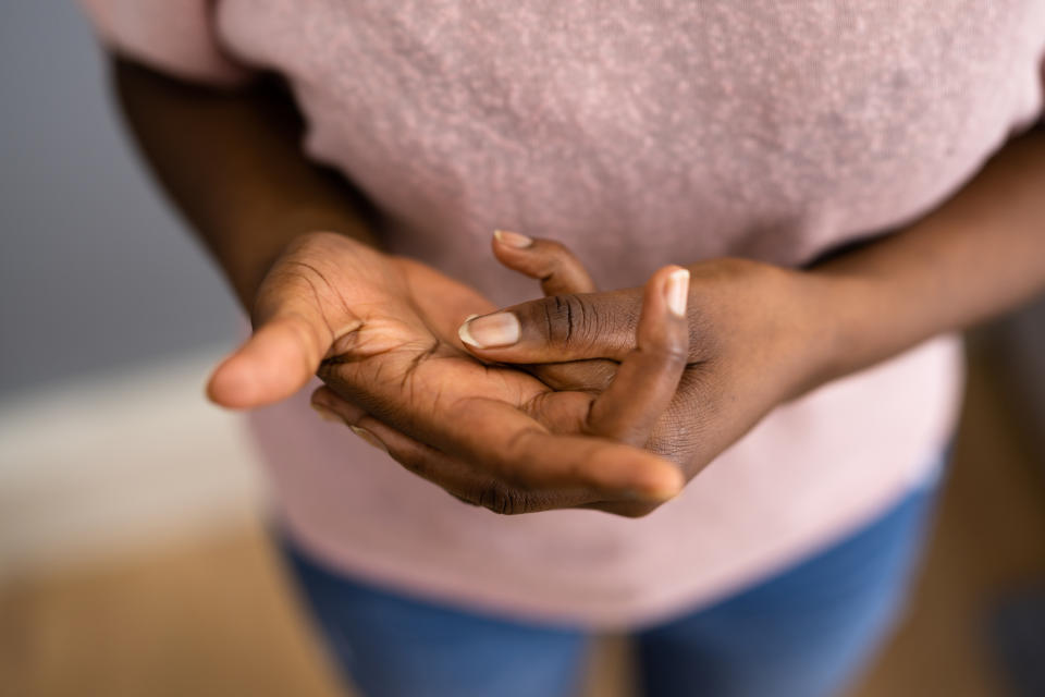 A person stands with hands clasped together, focusing on their fingers. Their attire consists of a plain shirt and jeans