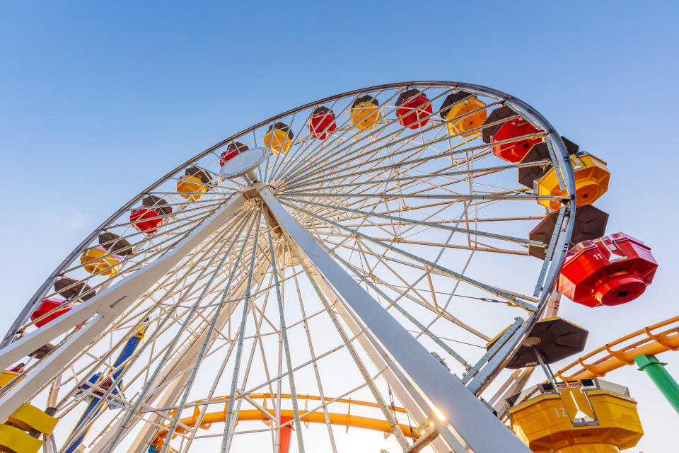 Ferris wheel with colorful cabins at an amusement park, viewed from below against a clear sky