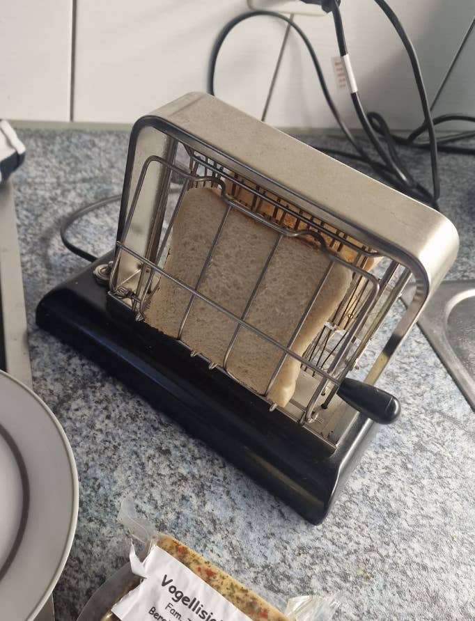 A vintage toaster on a kitchen counter holds two slices of bread. A package of bread is nearby