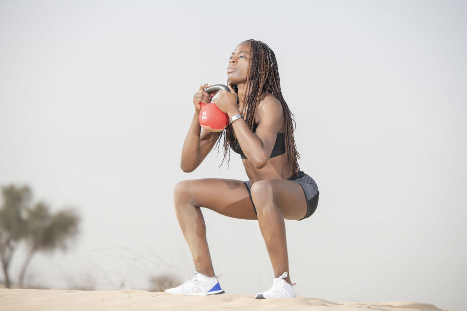 Person in athletic gear doing a squat with a kettlebell outdoors