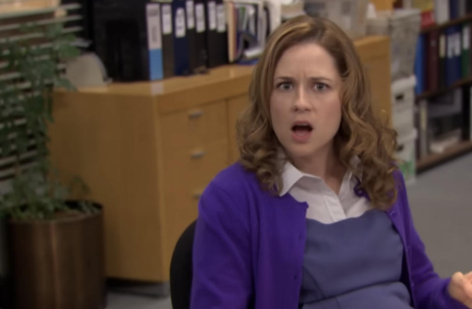 A woman in an office setting looks surprised, wearing a cardigan over a collared shirt. Office supplies are visible in the background