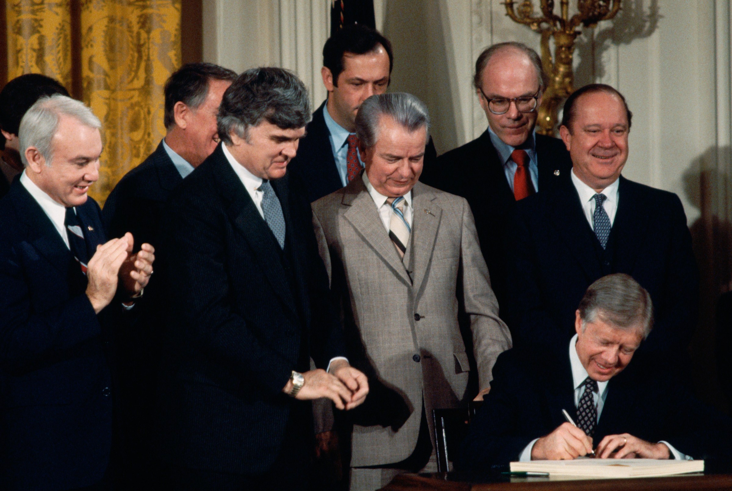 Carter signs the Windfall Profits Tax Bill as senators and representatives who helped it pass look on in 1980.