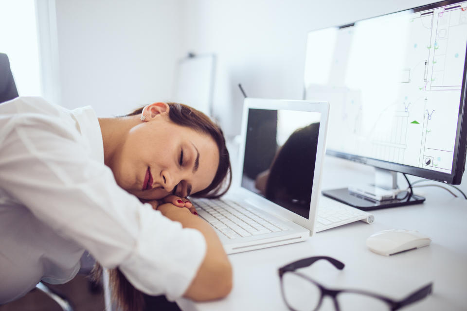Person sleeping on a desk with laptops and a monitor. Glasses and a mouse are nearby, suggesting exhaustion or a break during work