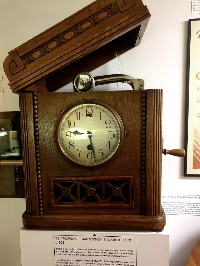 Vintage Tempophone gramophone alarm clock from 1925 with a wooden case and clock face, displayed in a museum setting