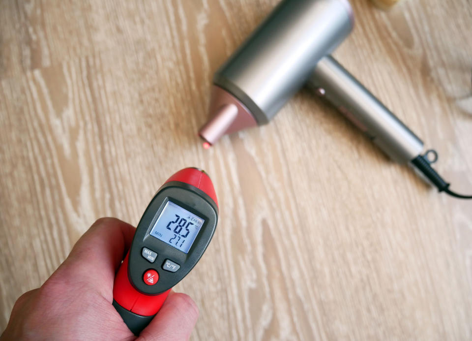 Hand holding a device reading 209.7, with a hairdryer in the background on a wooden surface