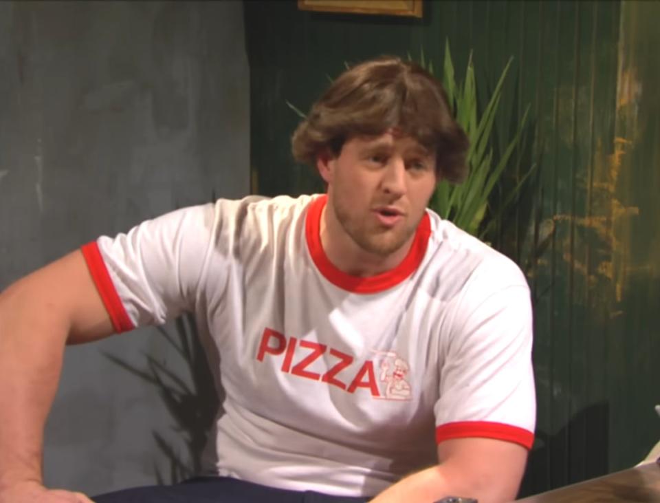 A man sitting at a table wearing a white t-shirt with the word &quot;PIZZA&quot; printed on it in red letters