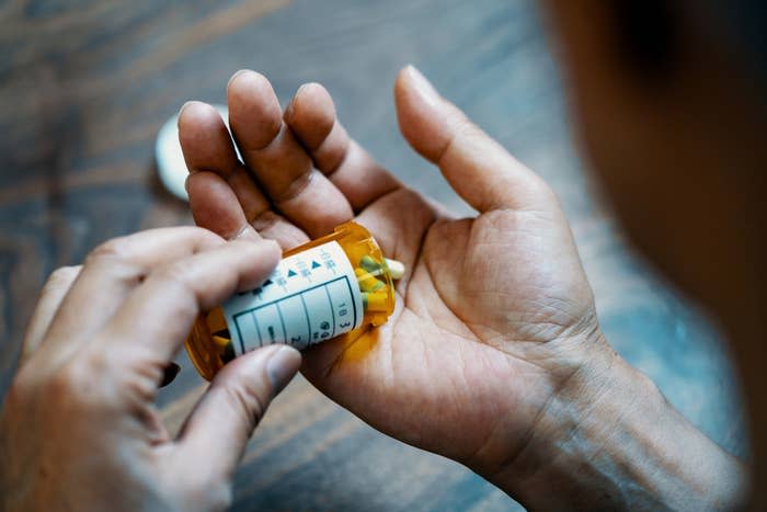 A person dispenses pills from an orange prescription bottle into their hand