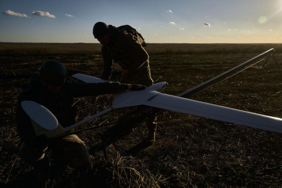 Two people handling a drone on a stand in a field.