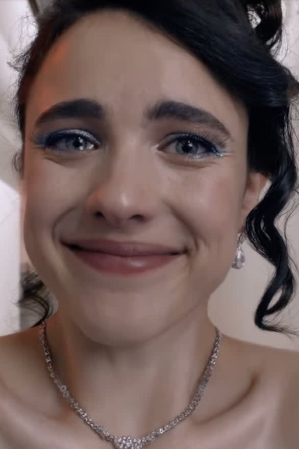 Person smiling with tearful eyes in a hallway, wearing a strapless top and a necklace. Hair is styled in an updo