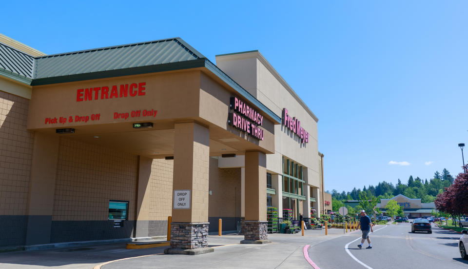 Pharmacy drive-thru entrance of a grocery store with a person walking in the parking lot