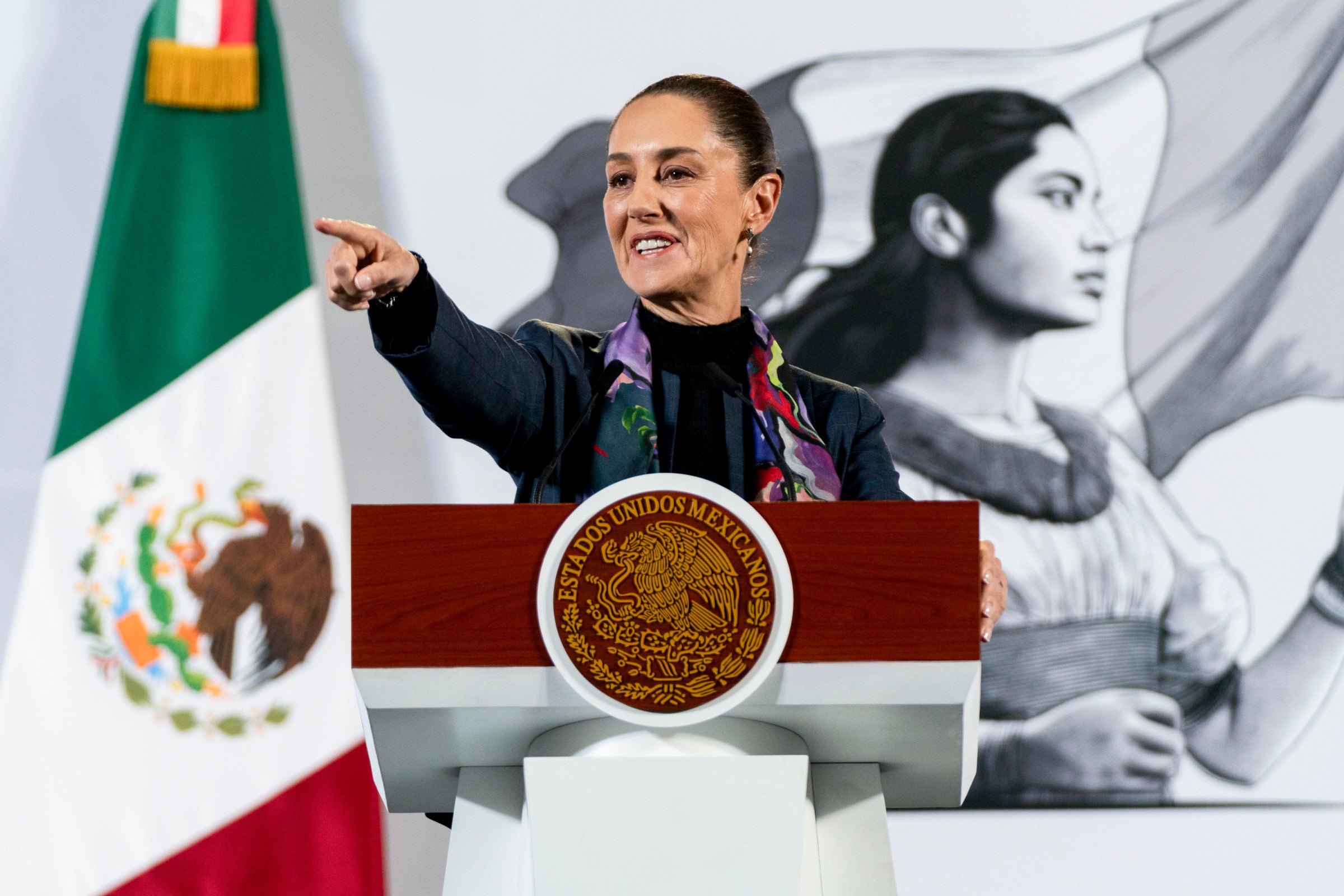 A woman politician speaking at a podium next to a Mexican flag