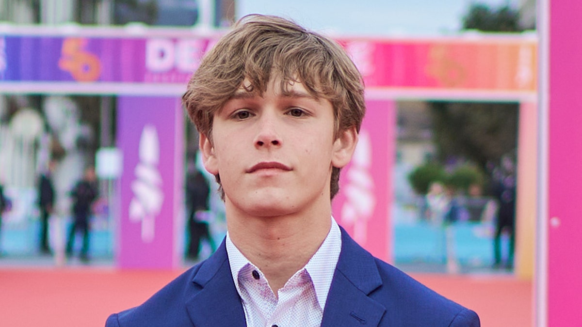 Hunter Meek stands tall on the carpet wearing a blue jacket and patterned button down shirt