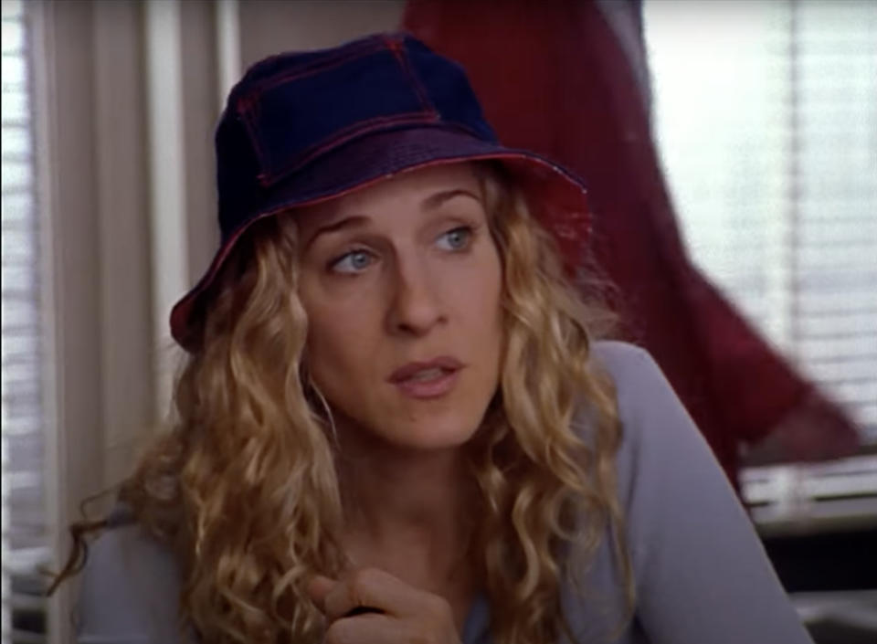 From &quot;Sex and the City&quot;: Sarah Jessica Parker wearing a casual outfit and a bucket hat, sitting indoors and looking to the side with an unsure expression