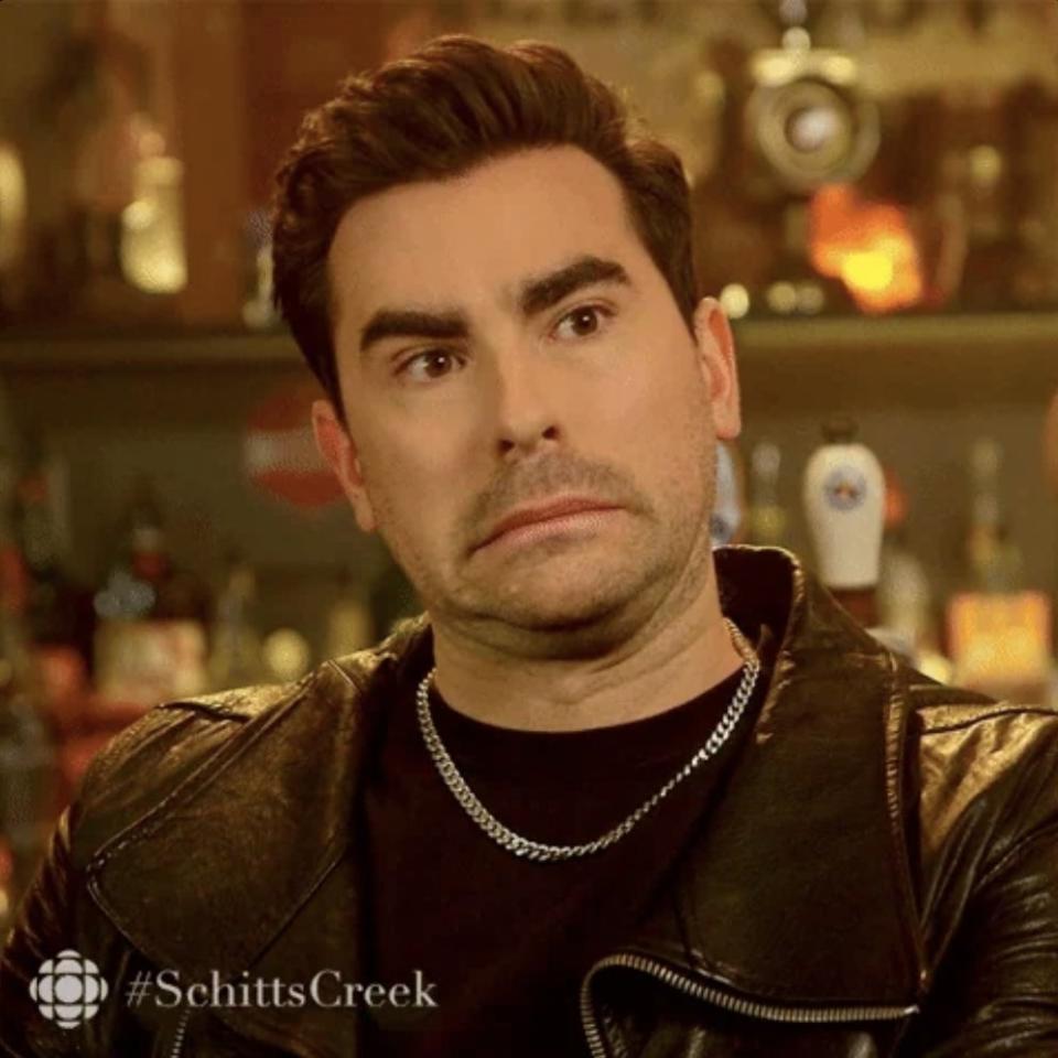 A person with a surprised expression in a bar, wearing a leather jacket and chain necklace. TV show logo in the corner