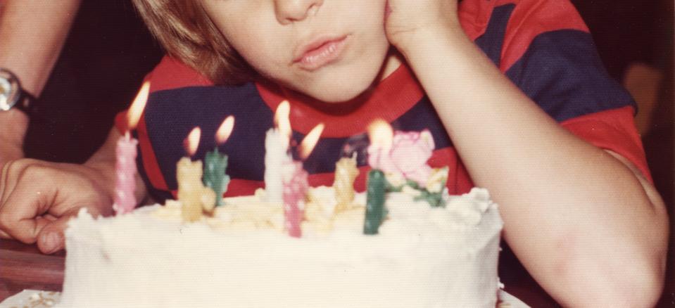 Vintage photo of a child with a thoughtful expression looking at a birthday cake with lit candles