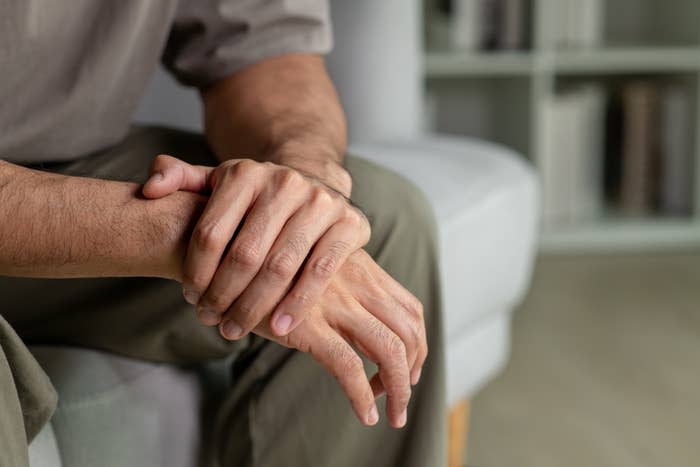 A person sitting on a couch, gently holding their wrist, conveying a sense of heavy contemplation