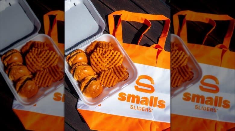 Smalls Sliders burgers and waffle fries in container, sitting on top of Smalls Sliders tote bag