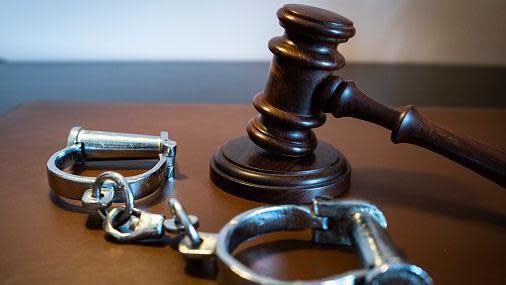 stock photo of a gavel and handcuffs on a leather surface
