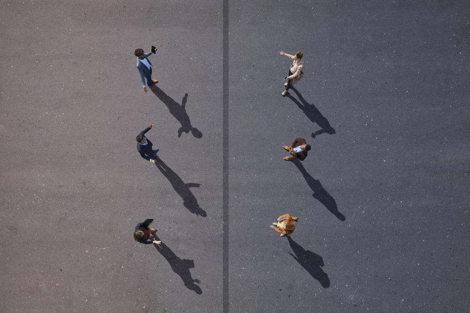 People walking in different directions, casting long shadows, viewed from above. Outdoor meeting or busy plaza vibe