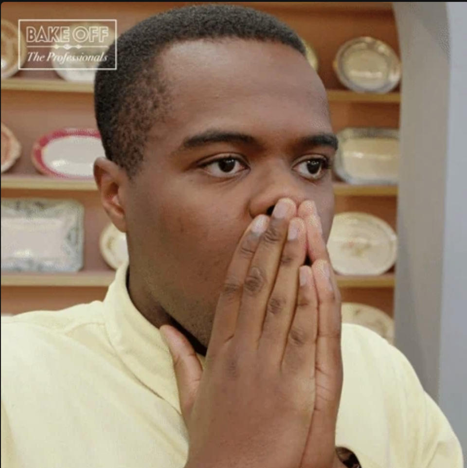 Person holding hands over face, looking surprised in a kitchen setting with plates on display in the background