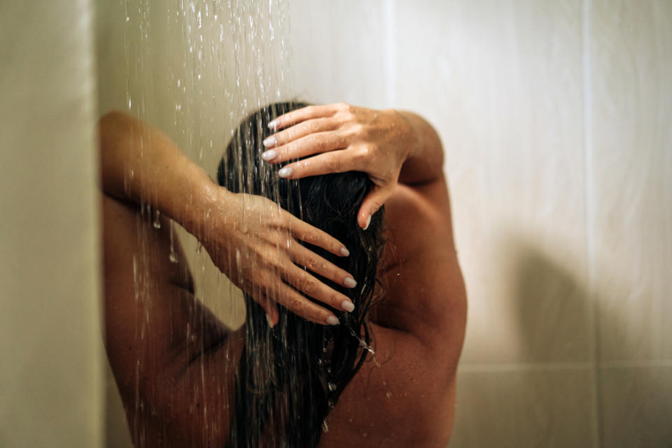 Person with their back to the camera stands under a shower, hands on their head, water pouring down