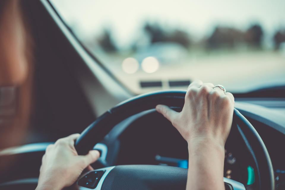 A person driving a car, hands on the steering wheel, with blurred road in the background