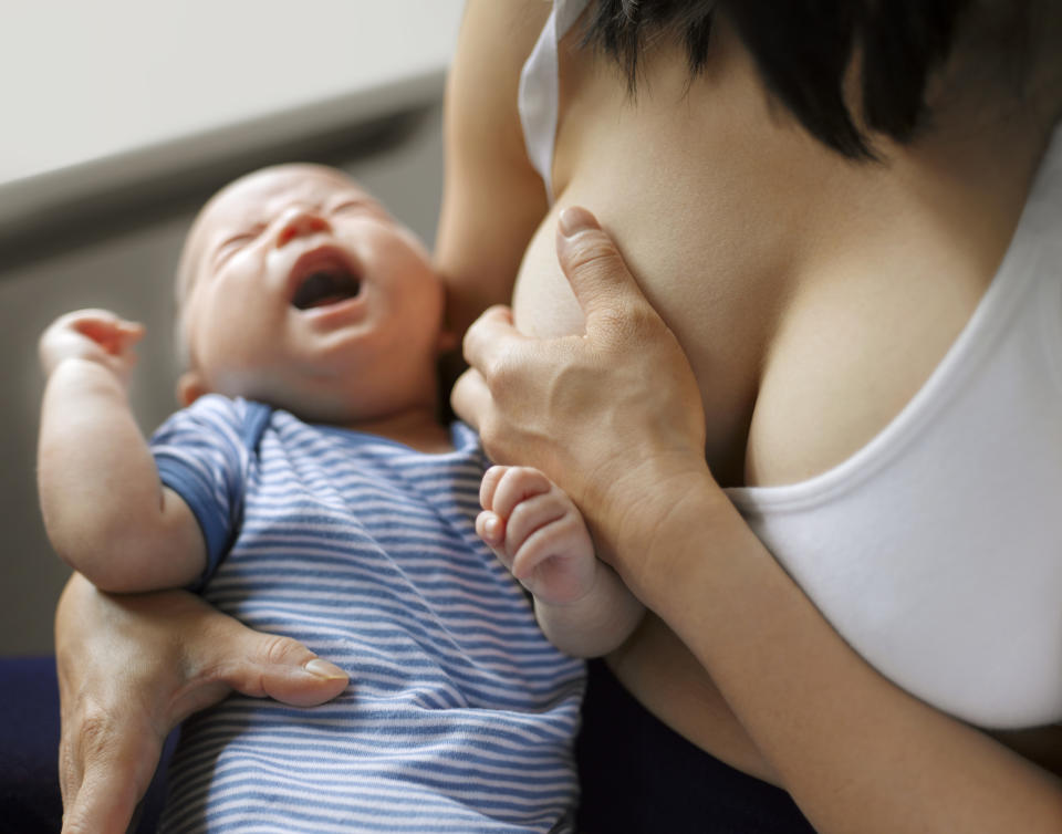 Person breastfeeding an infant wearing a striped outfit; the baby is crying