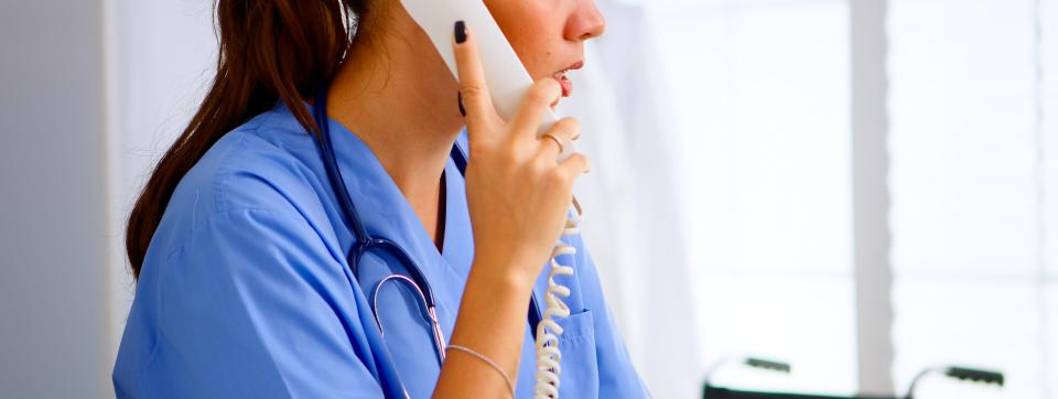 A healthcare professional in scrubs is talking on the phone in a medical setting, focused and attentive