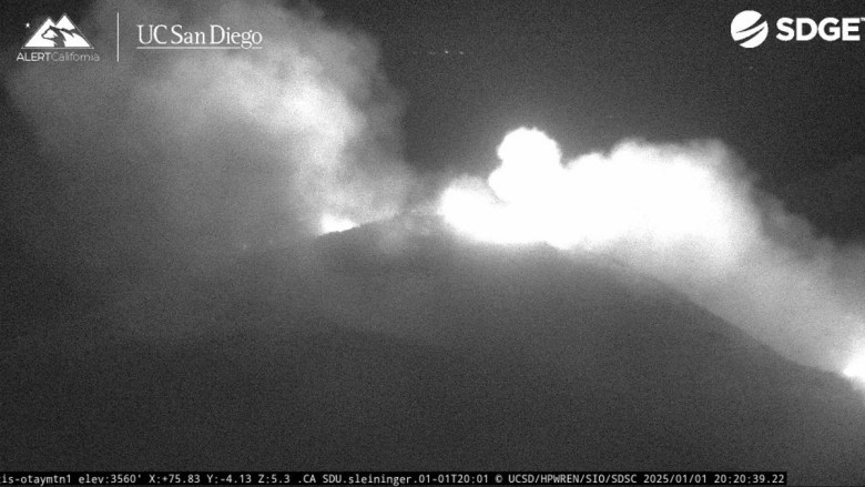 Black and white image of smoke and light over a mountain at night.