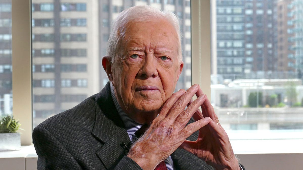 Jimmy Carter, hands clasped, wearing a suit appears on an ABC News tv series for one of his books