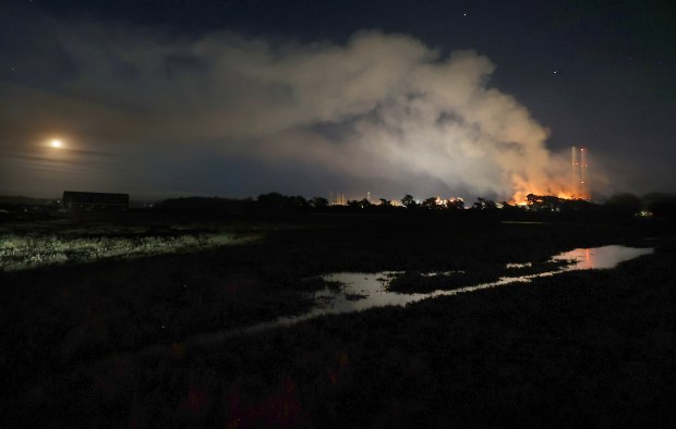 The moon rises over Elkhorn Slough as fire blazes Thursday...