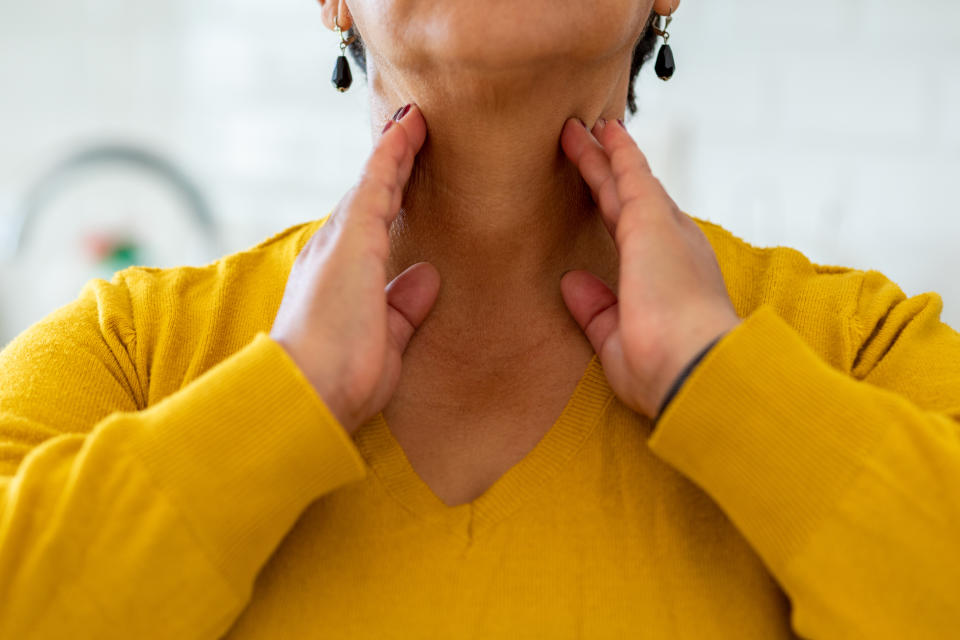 Person touching their neck, appearing to check for swelling or discomfort, wearing a sweater and earrings