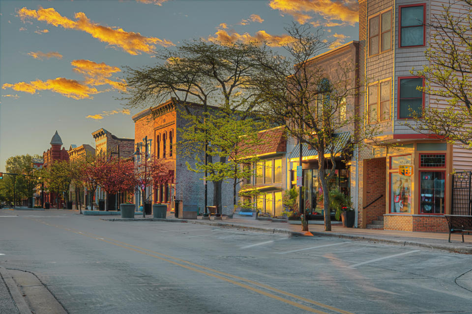 A quiet, picturesque small-town street lined with charming buildings and trees under a sunset sky