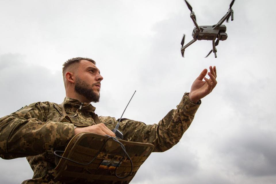 A man in camouflage releasing a small drone into the air.