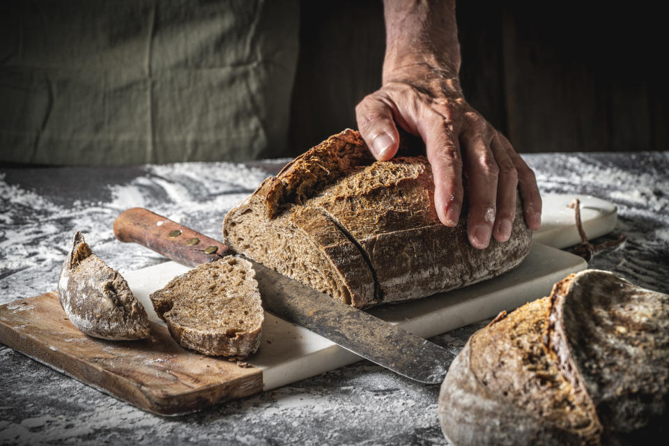 Male hands cutting Sourdough bread brown slices wholegrain homemade German style on cutting board with slices on white flour background