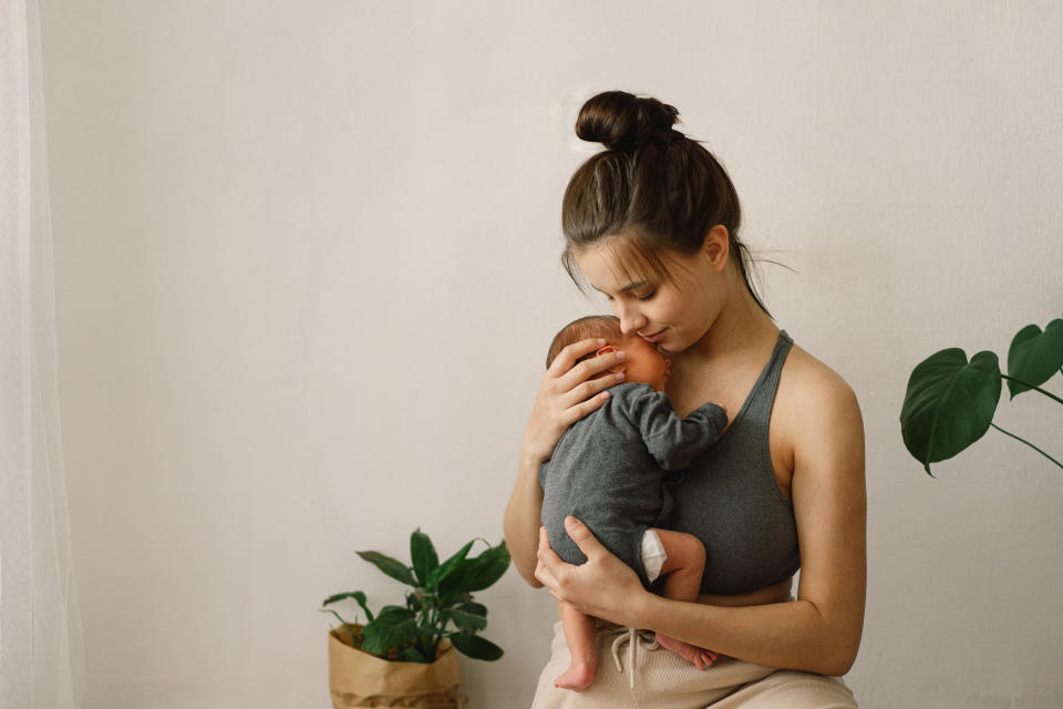 Woman gently holding a baby close to her chest, sitting beside a plant in a serene setting