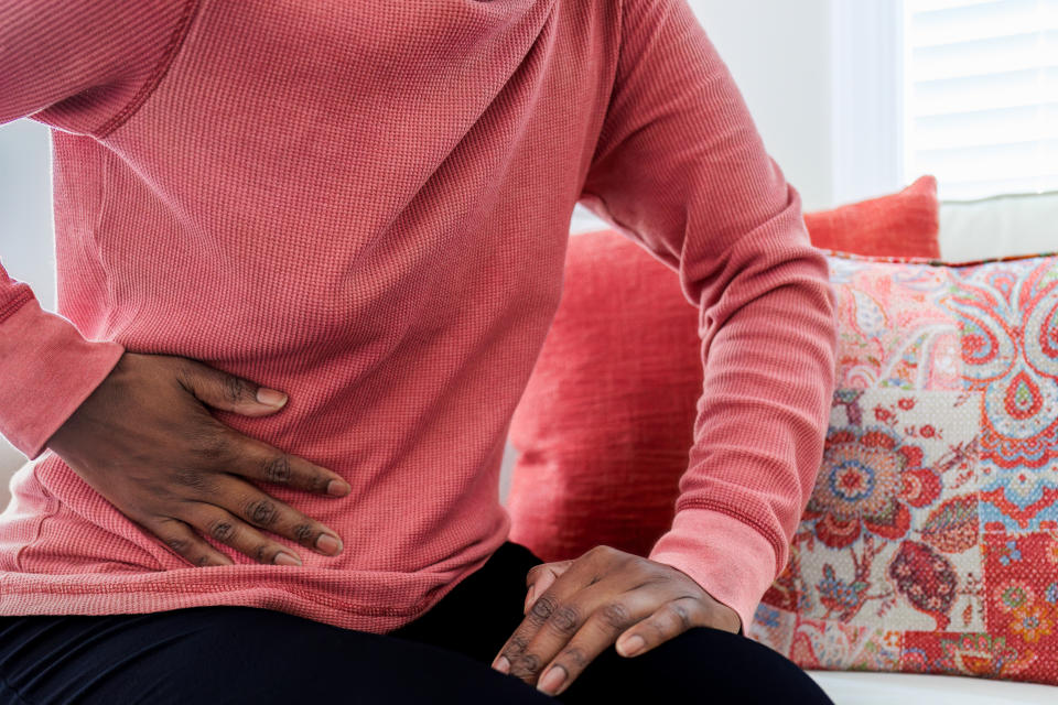 Person sitting on couch, holding stomach in discomfort, next to decorative pillows
