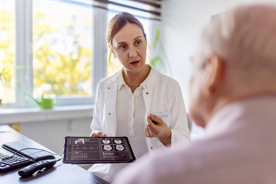 A doctor shows a tablet with medical information and x-rays to an elderly patient