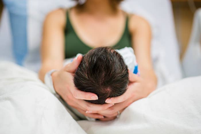 Person gently cradling a newborn's head, showing a nurturing moment in a hospital setting