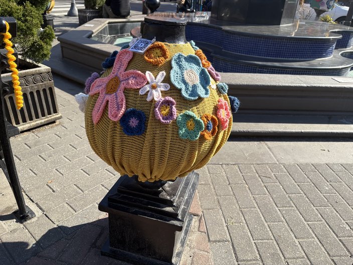 Knitted pink, blue, purple, orange and white flowers on top of an iron structure